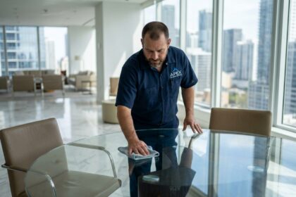 Technicien de nettoyage professionnel en uniforme soigné polissant une table en verre dans un bureau d'entreprise haut de gamme
