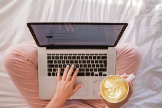 person using MacBook Pro and holding cappuccino
